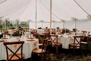 Romantische witte bruiloft tent ingericht in bohemian stijl, compleet met houten tafels en stoelen voor een romantisch huwelijksfeest in de buitenlucht