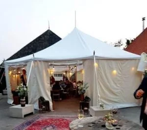 Sfeervol verlichte witte bruilofttent in Friesland met gesloten zijwanden; een feestelijke ambiance voor een onvergetelijk huwelijksfeest in de avonduren