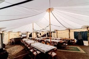 Warme ambiance in een bruilofttent; stijlvol gedekte tafels en comfortabele stoelen onder een sfeervol verlicht tentdoek