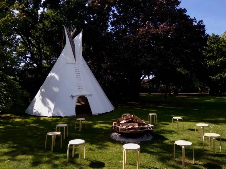 Tipi voor teambuilding op een grasveld met krukjes en een vuurschaal in een cirkel