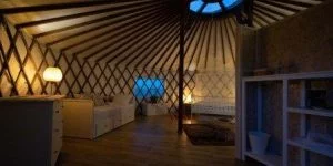 Sfeerverlichting in de yurt en een prachtig interieur met bed, kast en bank – door Windcirkeltenten Tiny house