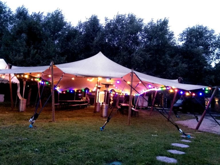 Feestelijk aangeklede stretchtent bij avond met sfeerverlichting, banken en tafels voor een tuinfeest - Locatie Hooge Zwaluwe - Windcirkeltenten