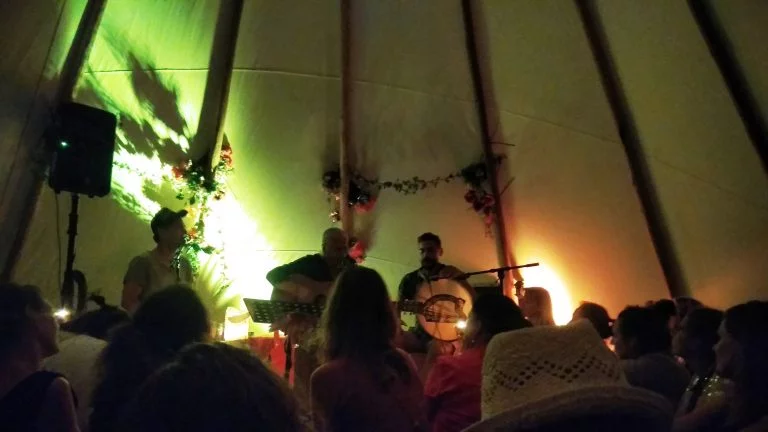 Sfeervol verlicht live muziek concert in een grote tipi tent op strand IJburg, Amsterdam; een unieke evenementen locatie aan het water bij avond