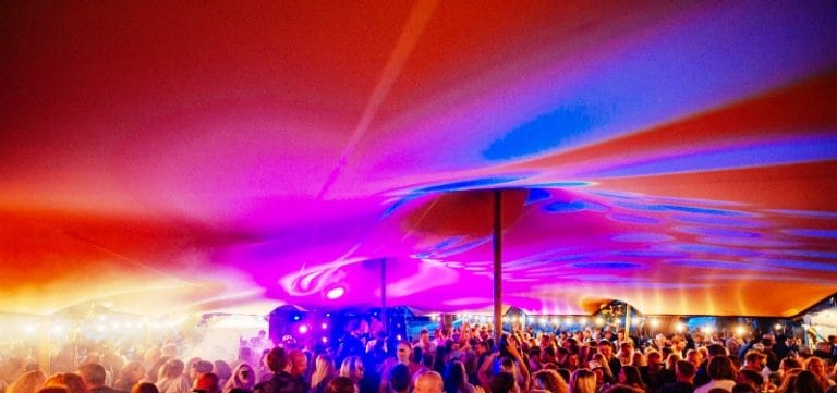 Sfeervol verlichte stretchtent met gekleurde lampen tijdens een avondfeest in de haven van Hoorn - Windcirkeltenten