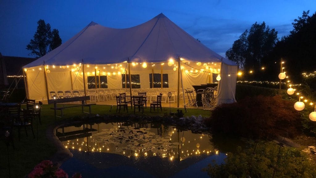 Luxe bruiloft tent in een tuin in Noord-Holland, in de schemering warm verlicht met sfeerverlichting en stijlvol ingericht met prachtig meubilair.