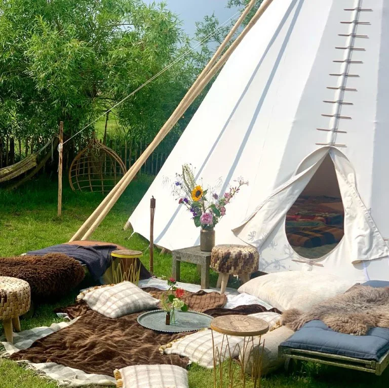 Prachtig opgestelde tipi tent voor feesten en evenementen, sfeervol ingericht met bloemen en zachte schapenvachten in de deuropening als uitnodigende setting